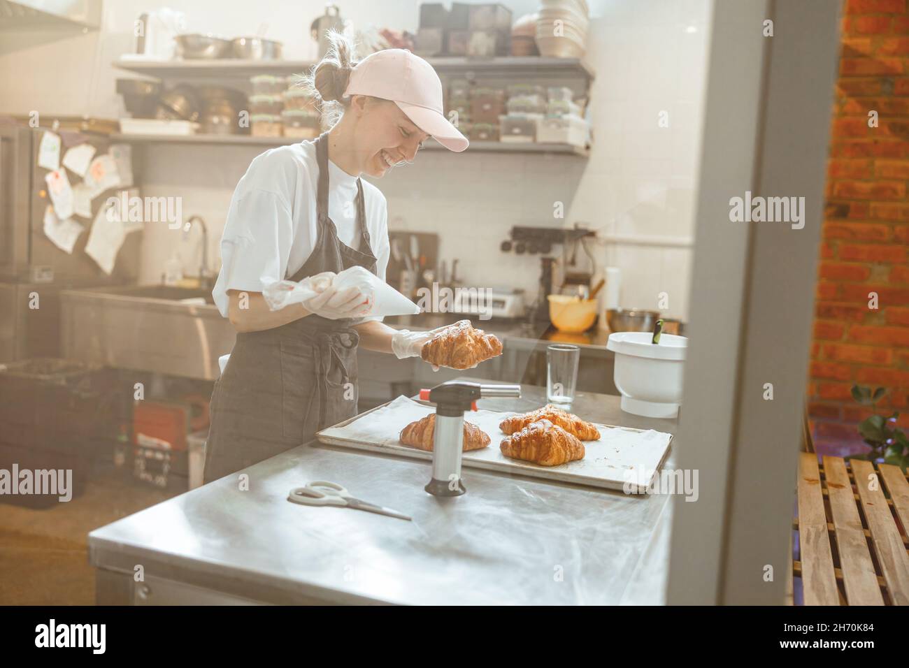 Positive Konditorei hält die Ärmel mit köstlicher Creme und Croissant in der Bäckerei Stockfoto
