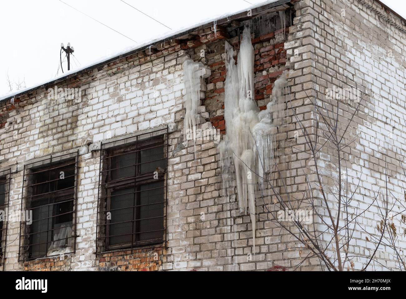 Eine alte zerstörte Mauer eines weißen Ziegelgebäudes mit Eiszapfen an einem frostigen Wintertag gegen einen grauen, düsteren Himmel. Selektiver Fokus. Nahaufnahme Stockfoto