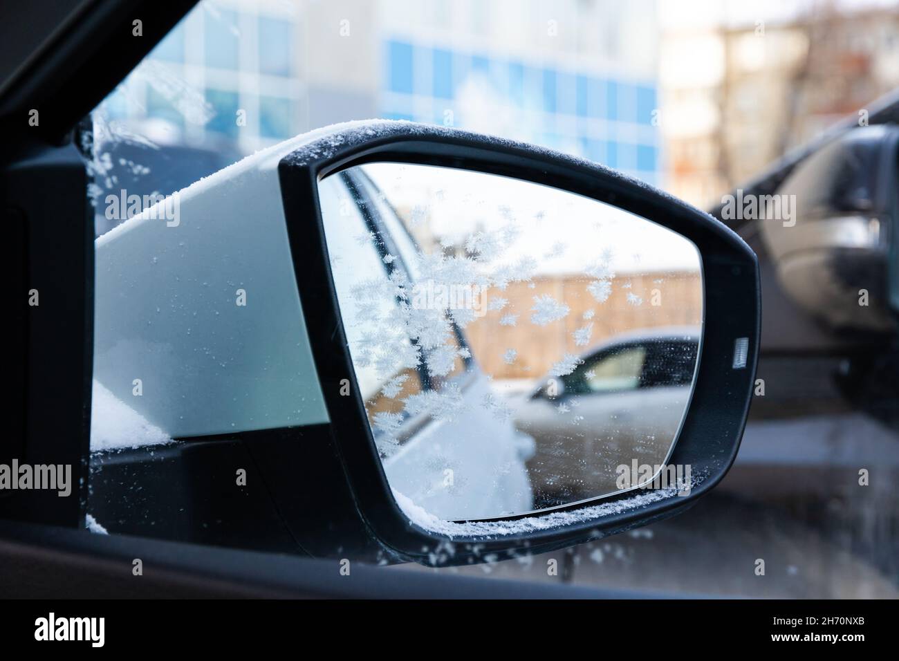 Seitenspiegel eines neuen weißen schneebedeckten Autos mit einer frostbedeckten Spiegelung an einem sonnigen, frostigen Tag im Ural. Selektiver Fokus. Nahaufnahme Stockfoto