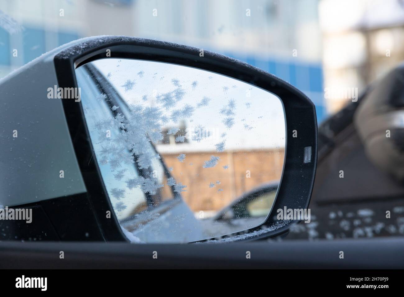 Seitenspiegel eines neuen weißen schneebedeckten Autos mit einer frostbedeckten Spiegelung an einem sonnigen, frostigen Tag im Ural. Selektiver Fokus. Nahaufnahme Stockfoto