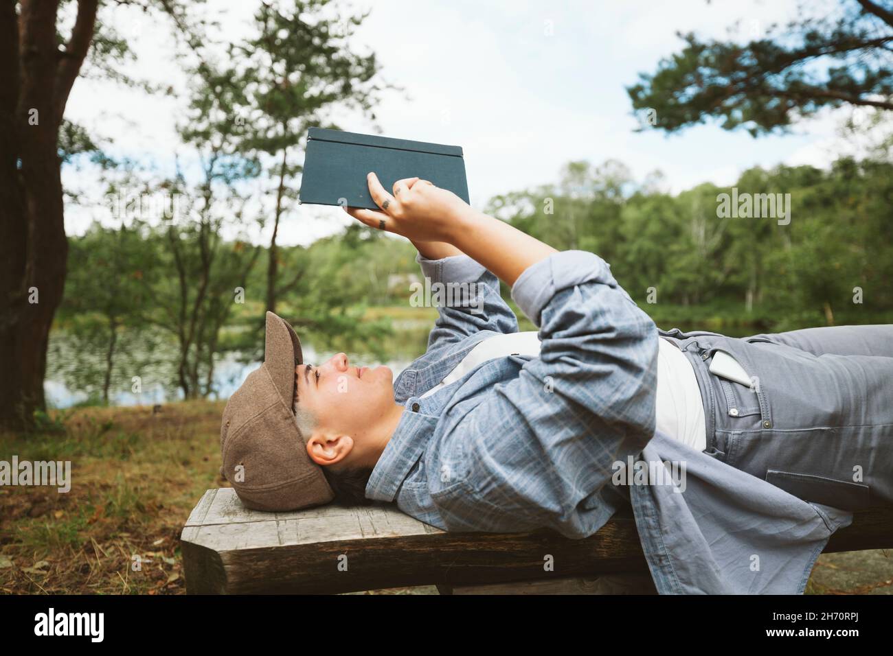 Junge Frau liest Buch, während sie auf einer Holzbank liegt Stockfoto