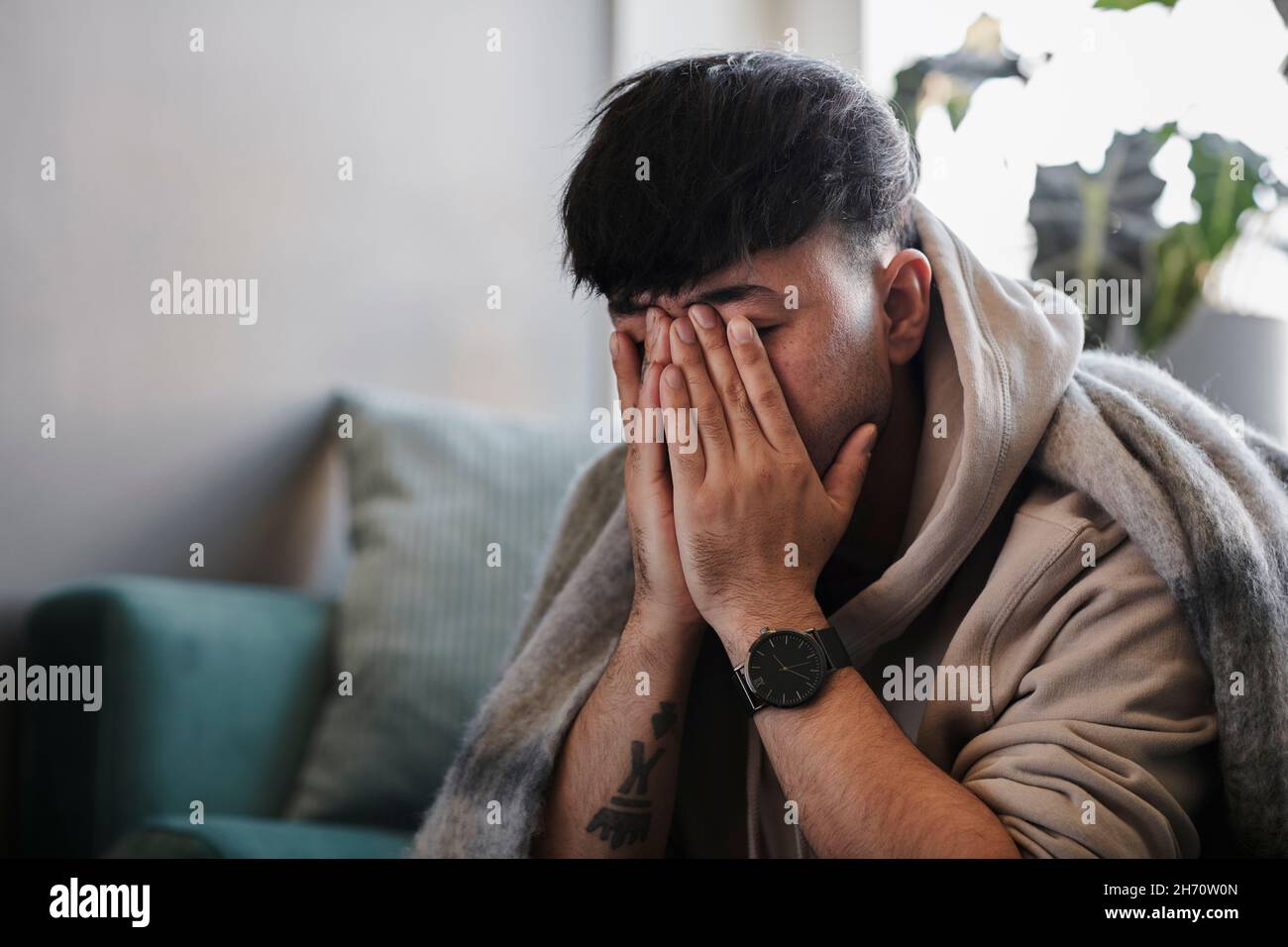 Kranker Mann auf dem Sofa mit Händen, die das Gesicht bedecken Stockfoto