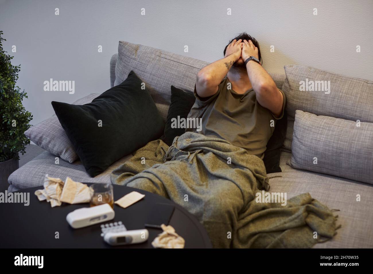 Kranker Mann auf dem Sofa mit Gesicht in den Händen Stockfoto