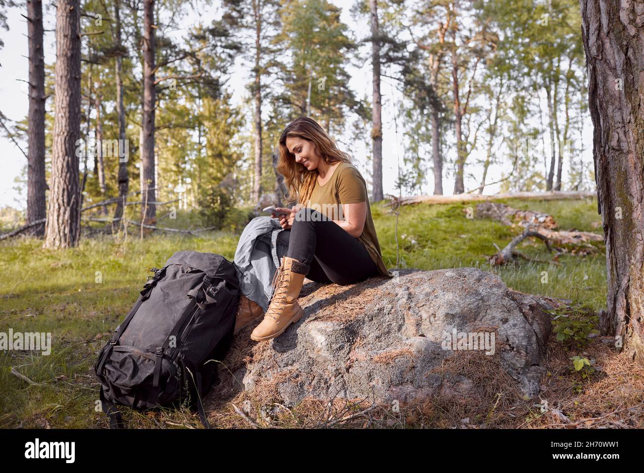 Frau, die auf Felsen sitzt und ein Handy benutzt Stockfoto