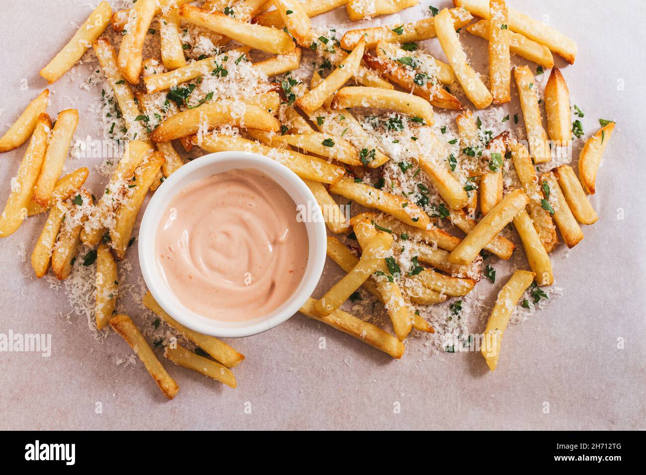 Pommes frites mit Parmesan und Petersilie und einer kleinen Schüssel rosafarbener Mayonnaise. Stockfoto