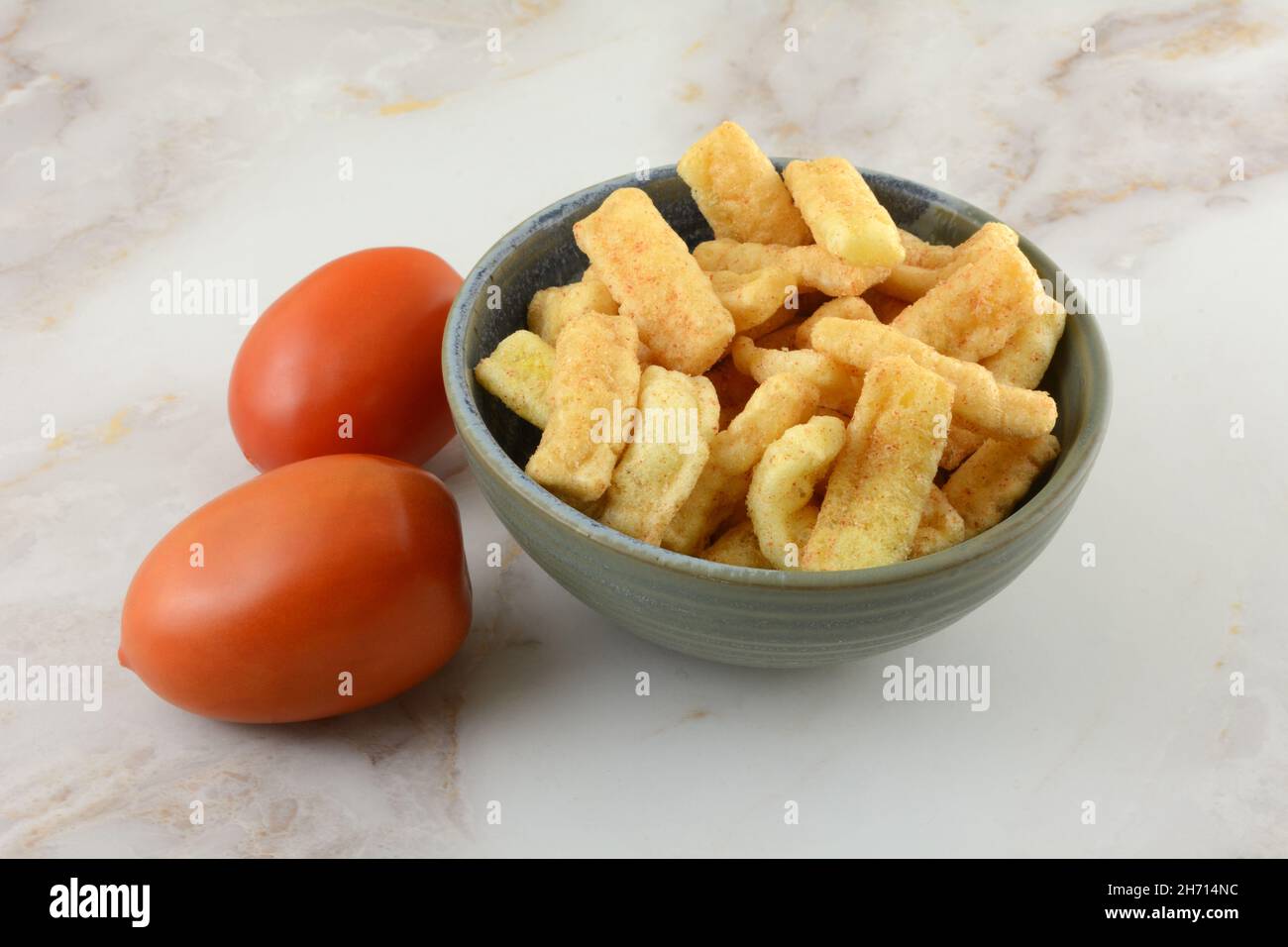 Würziger Mais-Snack mit Tomatengeschmack in einer Schüssel mit frischen rohen Tomaten Stockfoto