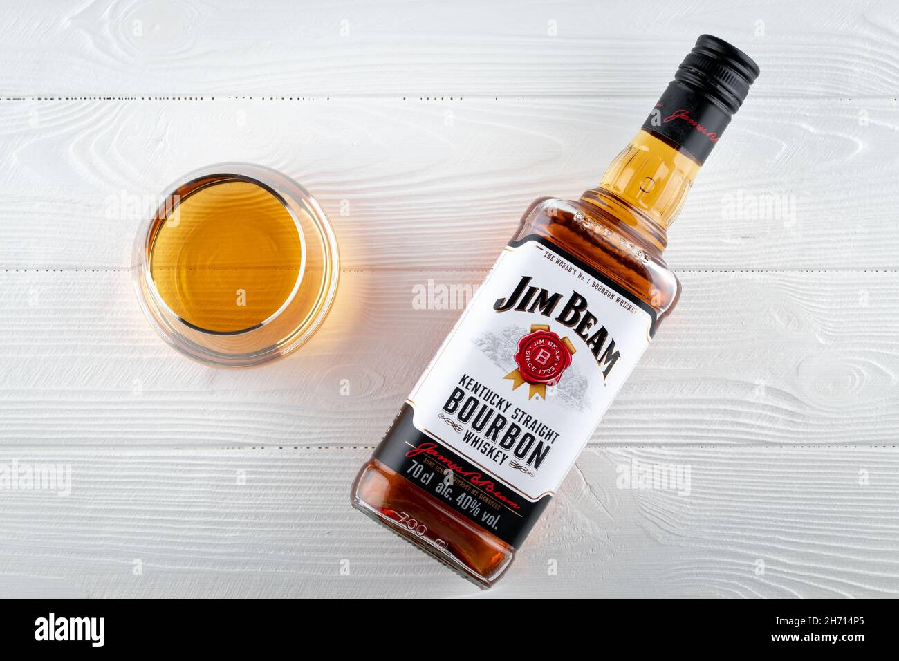 Volle Flasche Jim Beam auf einem weißen Holztisch. Ein Glas Bourbon. Starkes Getränk. Alte Whiskey-Marke. Draufsicht. Illustratives Editorial Stockfoto