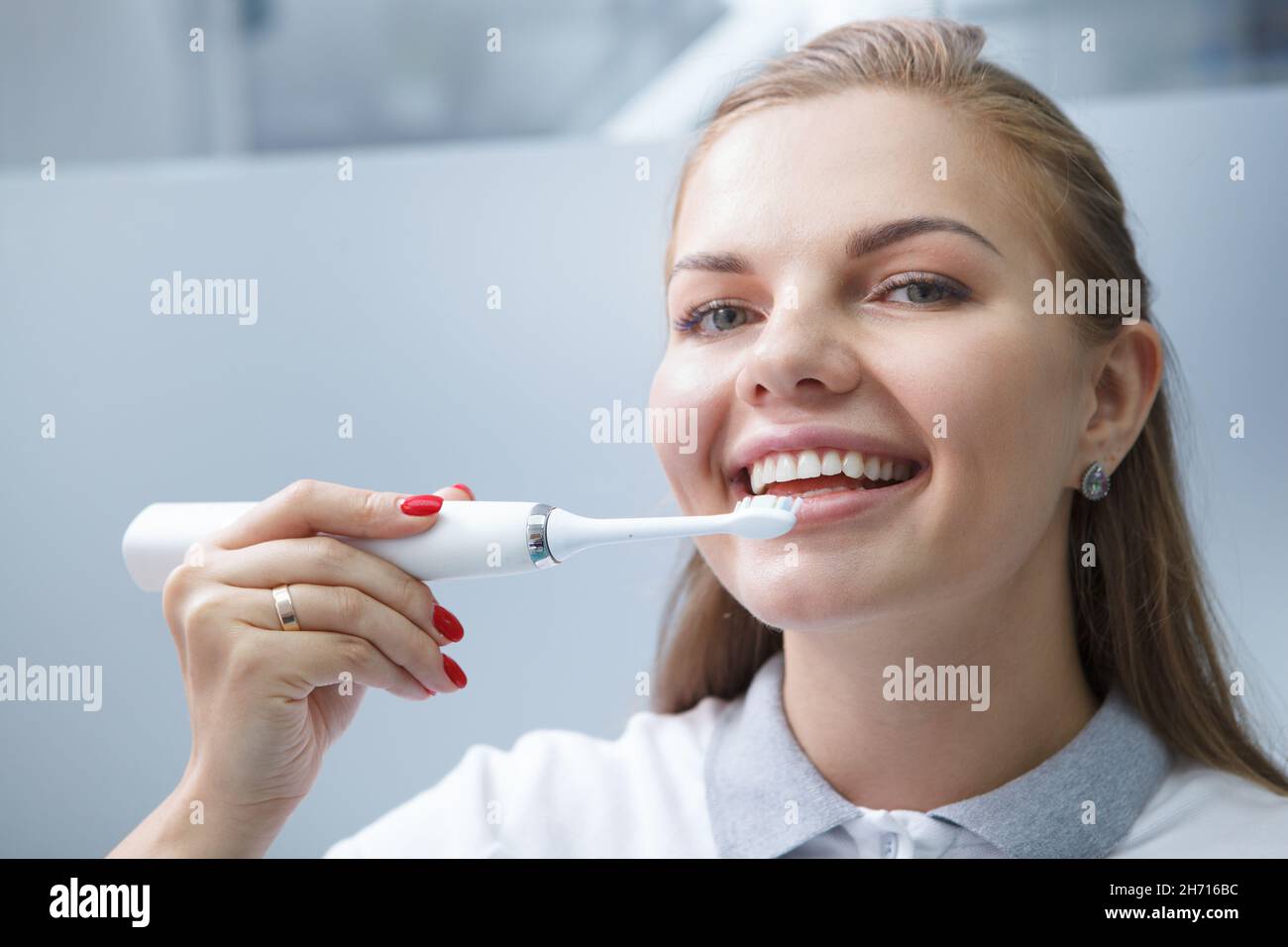 Nahaufnahme einer charmanten jungen Zahnärztin, die lächelt und eine elektrische Zahnbürste an ihren Zähnen verwendet Stockfoto