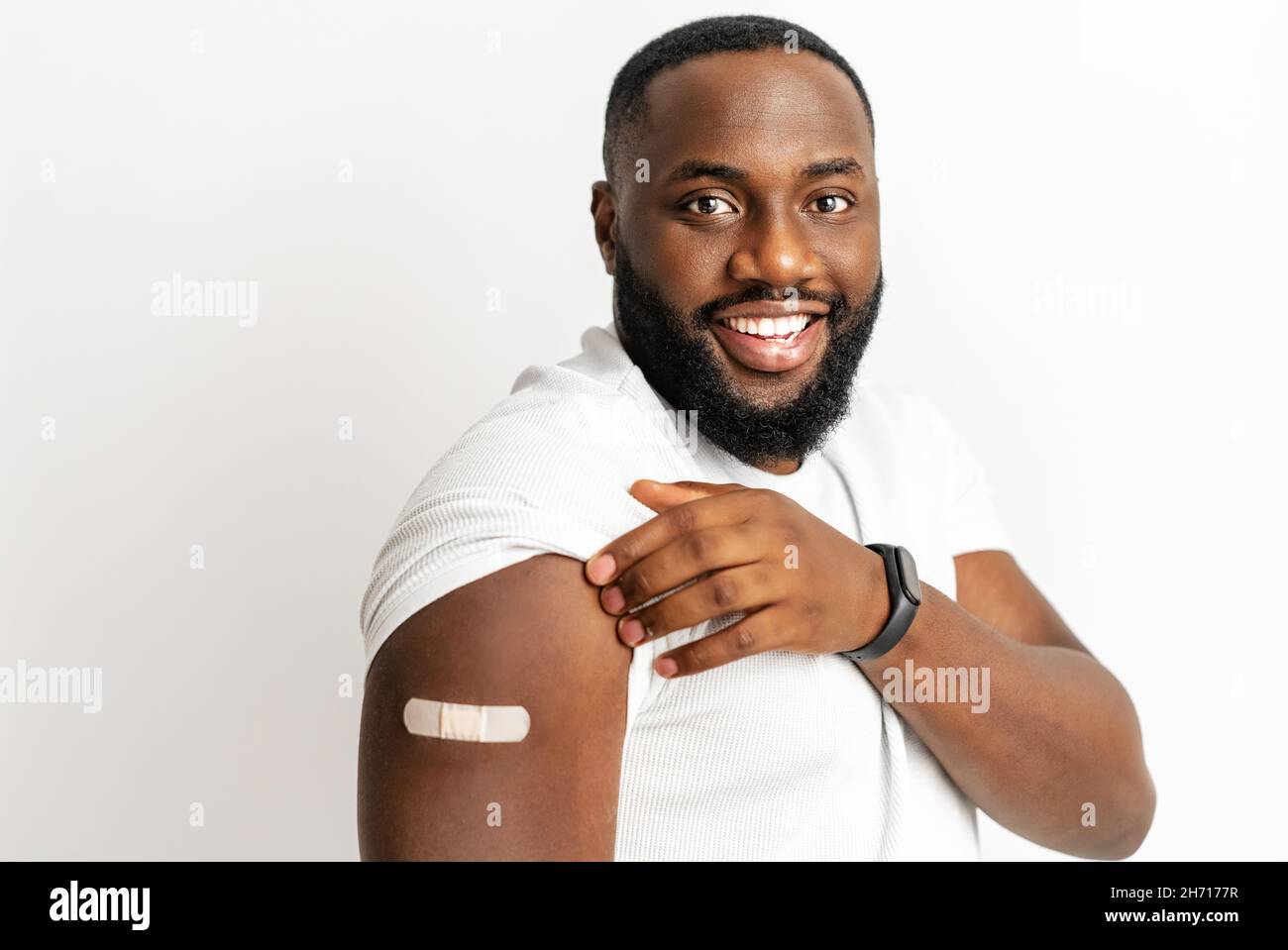 Fröhlicher, geimpfter afroamerikanischer Mann, der Arm mit medizinischem Pflaster zeigt und lacht, schwarzer Mann erhält Impfdosis gegen Covid, Gips auf der Schulter, isoliert auf Weiß. Gesundheitskonzept Stockfoto