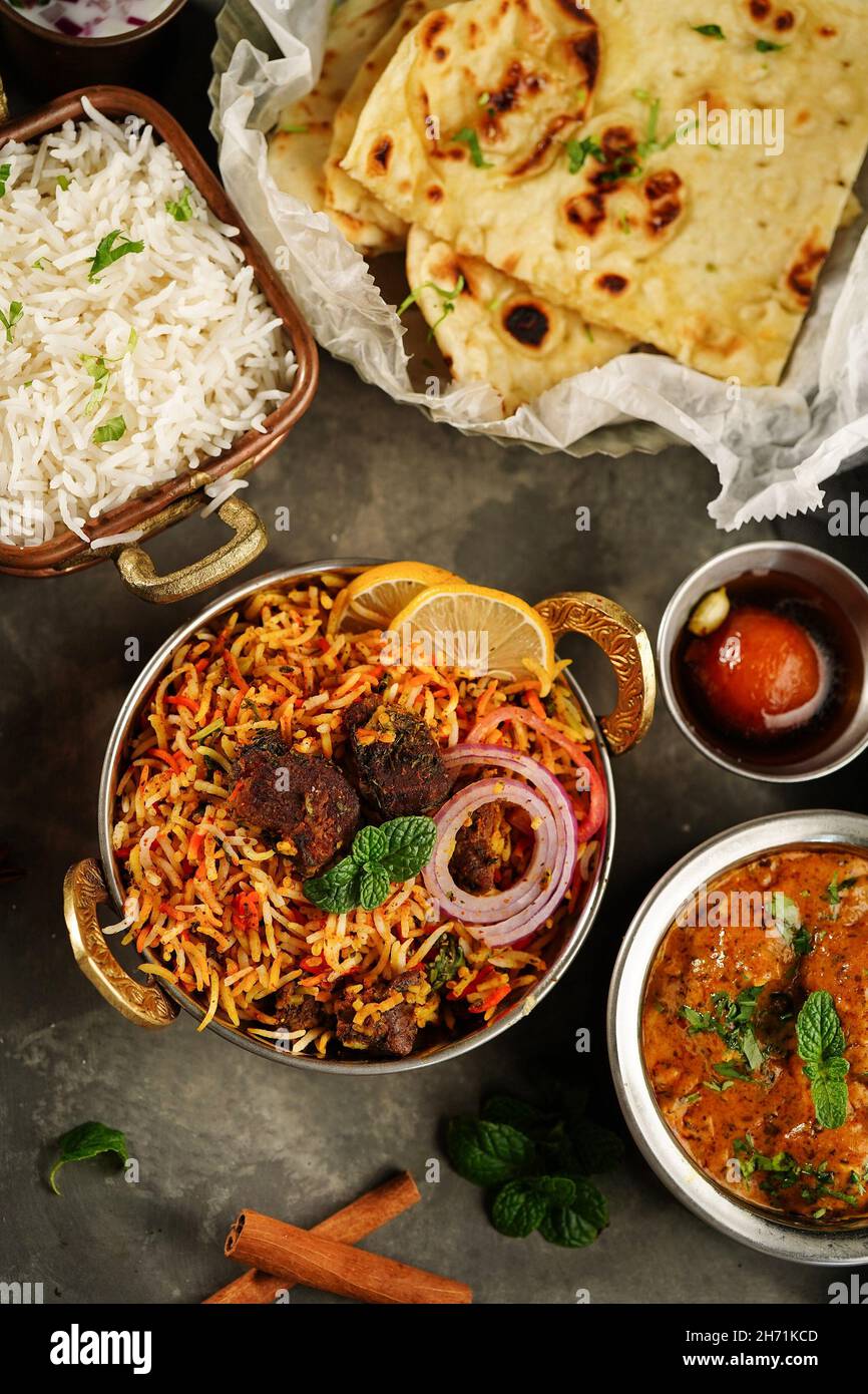 Indische Mahlzeit Thali - Hammelfleisch Biryani, Raita, Malai Kofta, Basmati-Reis, Butter Naan und Gulab Jamun auf einem Tablett serviert Stockfoto