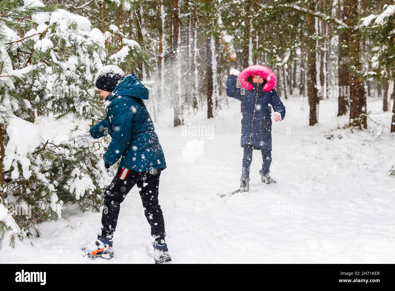 Der Junge schwingt einen Schneeball mit einem Mädchen. Lustige Kinder im Winter Park spielen Schneebälle und verbringen aktiv Zeit im Freien. Winter verschneiten Wald. Kalt Stockfoto