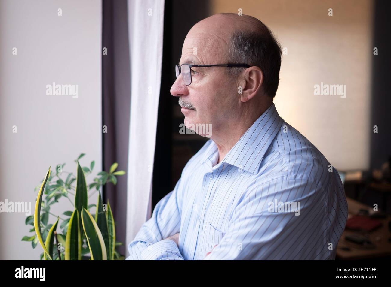 Älterer kaukasischer Mann, der einsam aus dem Fenster schaute Stockfoto