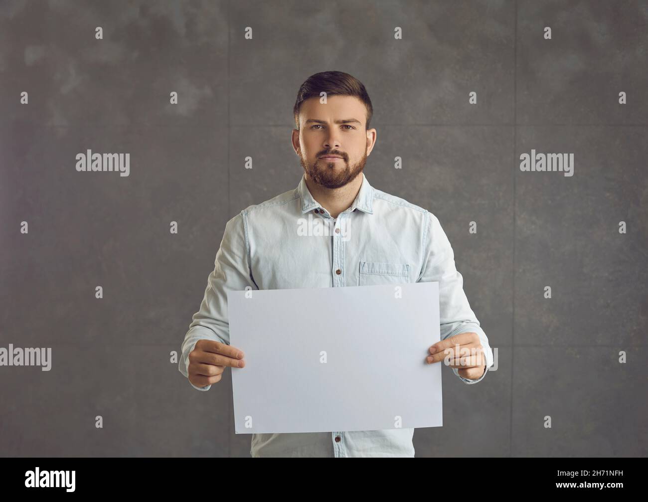 Junger Mann, mit einem Bart, hält ein leeres Blatt Papier, ernst. Stockfoto