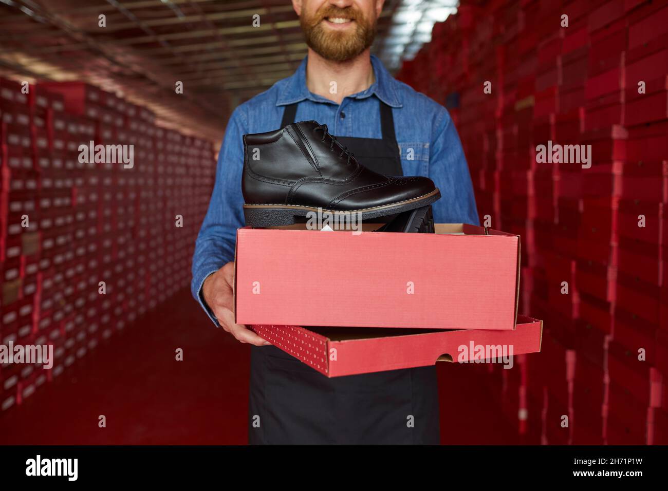 Lagerarbeiter oder Besitzer einer Schuhfabrik, die einen neuen schwarzen Lederstiefel zeigt Stockfoto