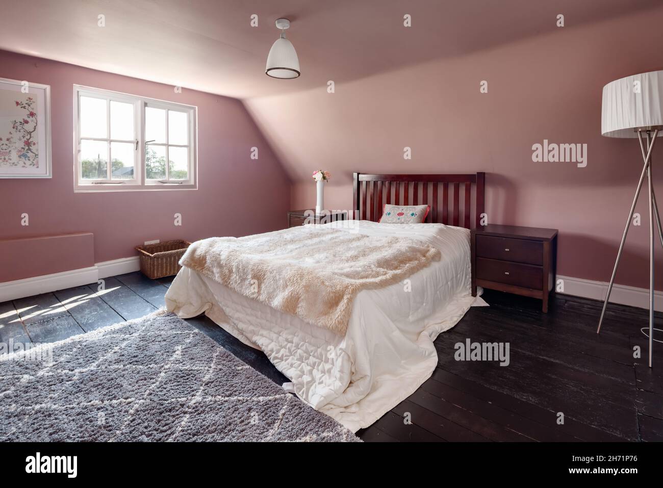 Ashdon, England - Juli 25 2019: Gut proportioniertes Schlafzimmer mit Doppelbett, Sonnenlicht durch Fenster und auffallend rosa Wänden. Stockfoto