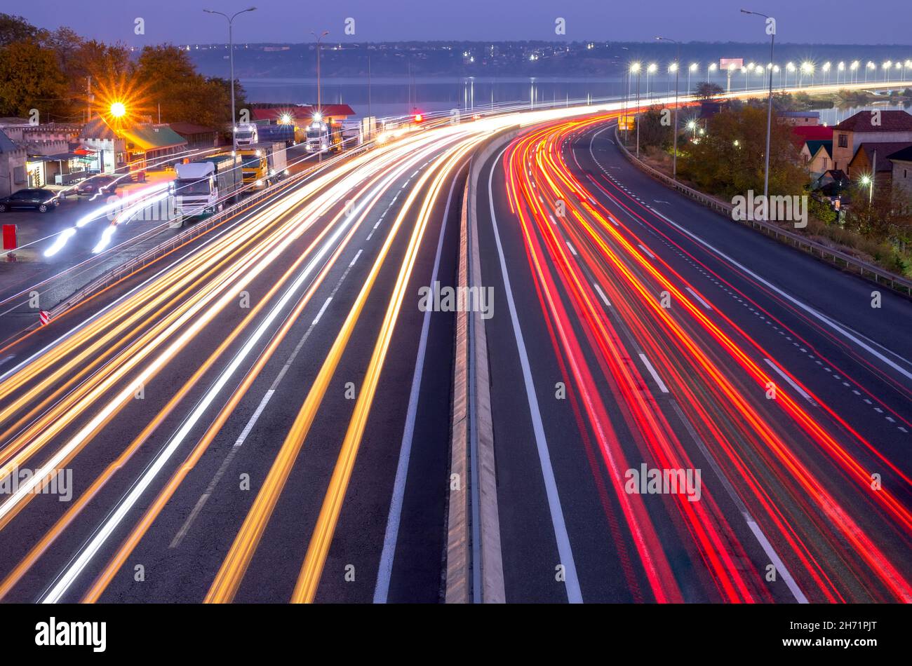 Vorstadtautobahn am Abend. Spuren von Scheinwerfern und Schlussleuchten von starkem Verkehr und Ampeln auf der Brücke Stockfoto
