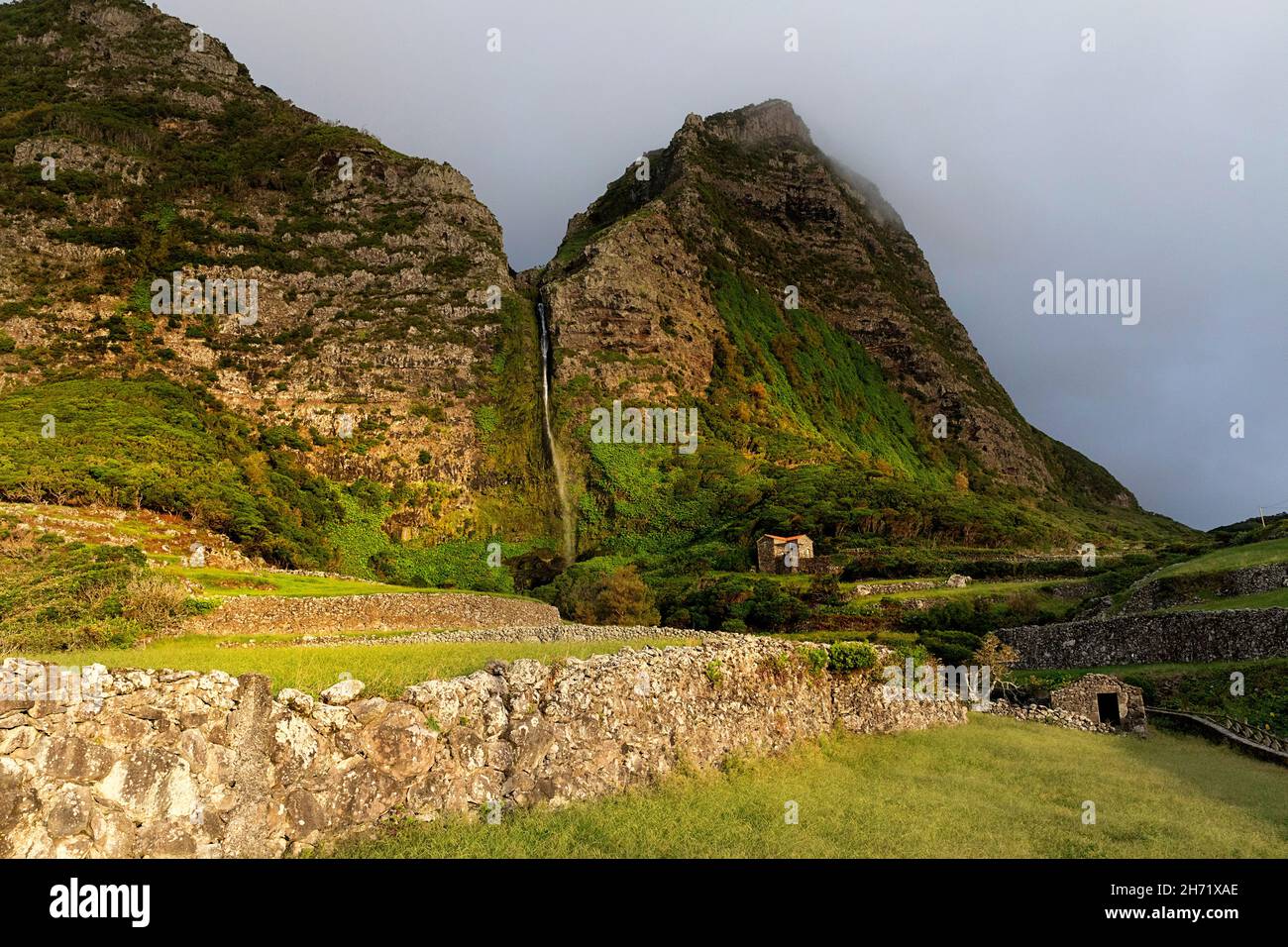 Steinmauer und Pfad zum Wasserfall Cascata do Poco do Bacalhau bei Sonnenuntergang, ein Steingebäude im Hintergrund, Faja Grande, Flores, Azoren Stockfoto