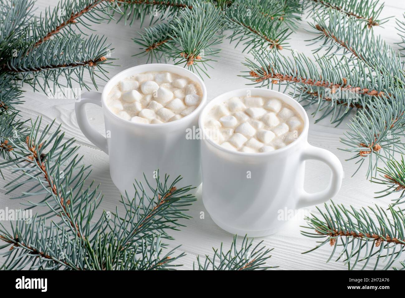 Zwei weiße Becher mit heißer Schokolade mit Marschall und Weihnachtsbaum auf weißem Holztisch. Kakao-Getränk am Morgen mit Neujahrsdekoration, Fichte Stockfoto