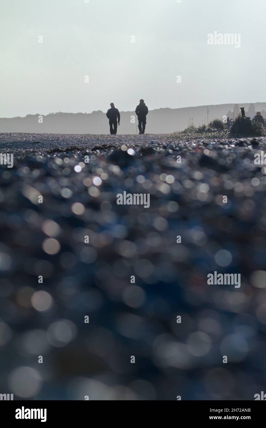 Zwei Personen, die im Winter am Strand bei Sonnenuntergang mit verschwommenem Vordergrund spazieren, Avon Beach Christchurch UK Stockfoto