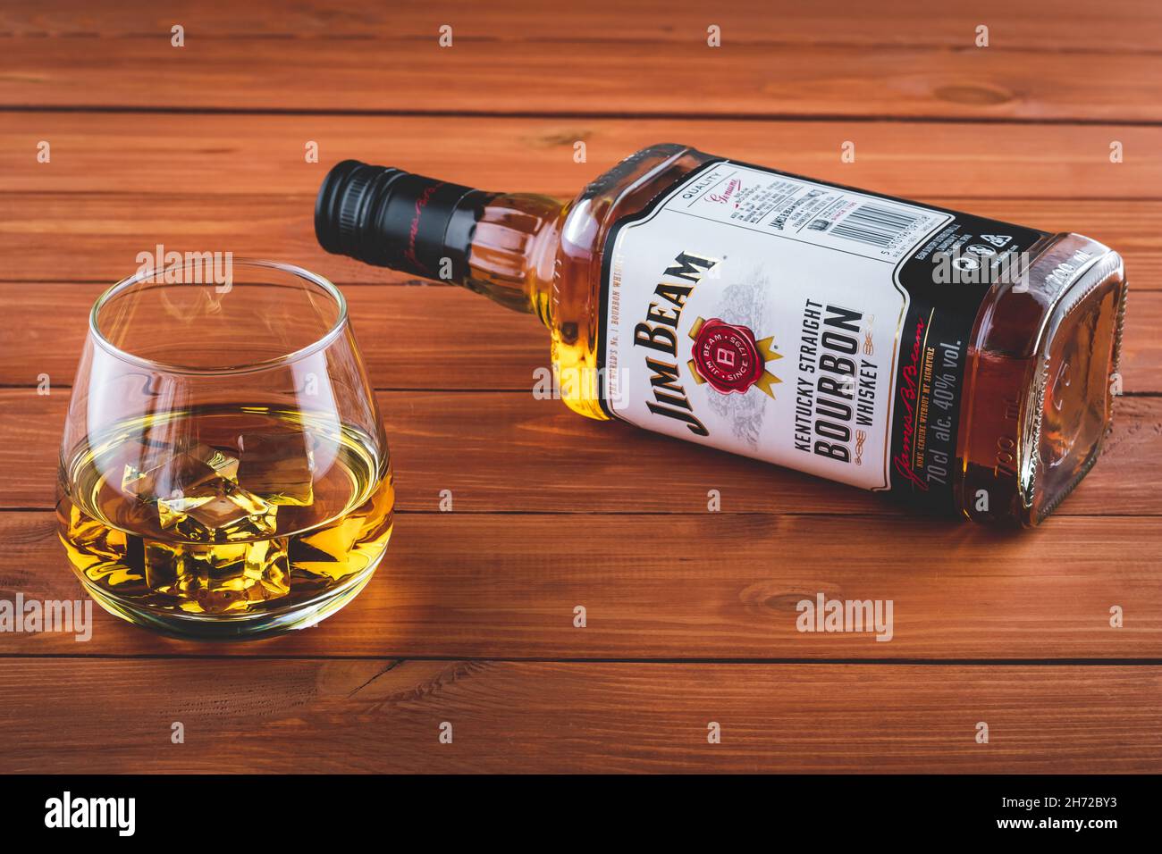 Eine Flasche Jim Beam auf einem braunen Holztisch. Ein Glas Bourbon mit Eis. Starkes Getränk. Alte Whiskey-Marke. Illustratives Editorial Stockfoto