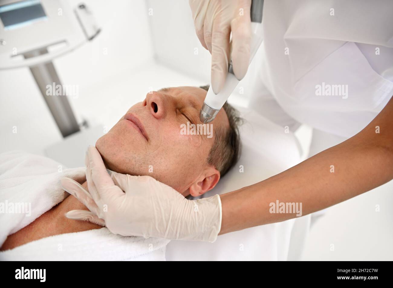 Kosmetologe macht Verfahren der Gesichtshaut eines schönen mittleren Alters 50 Jahre alt in einem Schönheitssalon. Kosmetik und professionelle Hautpflege conce Stockfoto