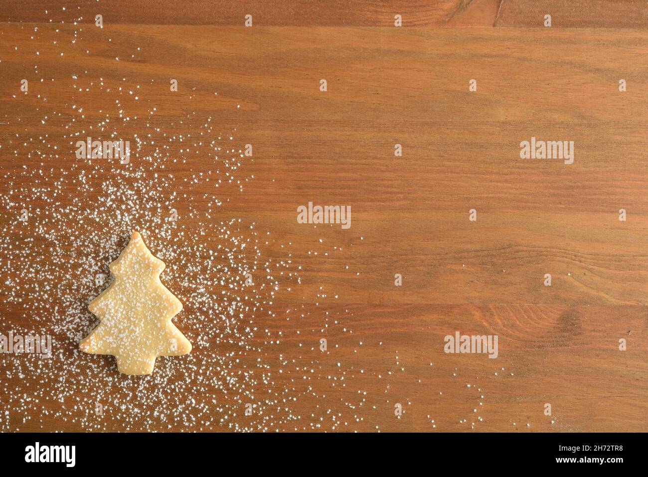 Weihnachtshintergrund mit tannenförmigen Keks in einer Ecke, bestreut mit Puderzucker auf Holzhintergrund. Draufsicht. Horizontale Zusammensetzung. Stockfoto