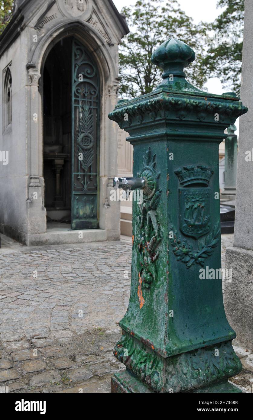 Auf einem Pfad in der Nähe eines Mausoleums auf dem historischen Friedhof Passy (Cimetière de Passy) in Paris steht ein gusseiserner Brunnen. Stockfoto
