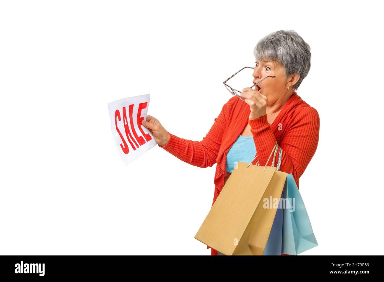 Ältere Frau, die überraschend einkauft, sieht sich das VERKAUFSSCHILD auf isoliertem weißem Hintergrund an Stockfoto