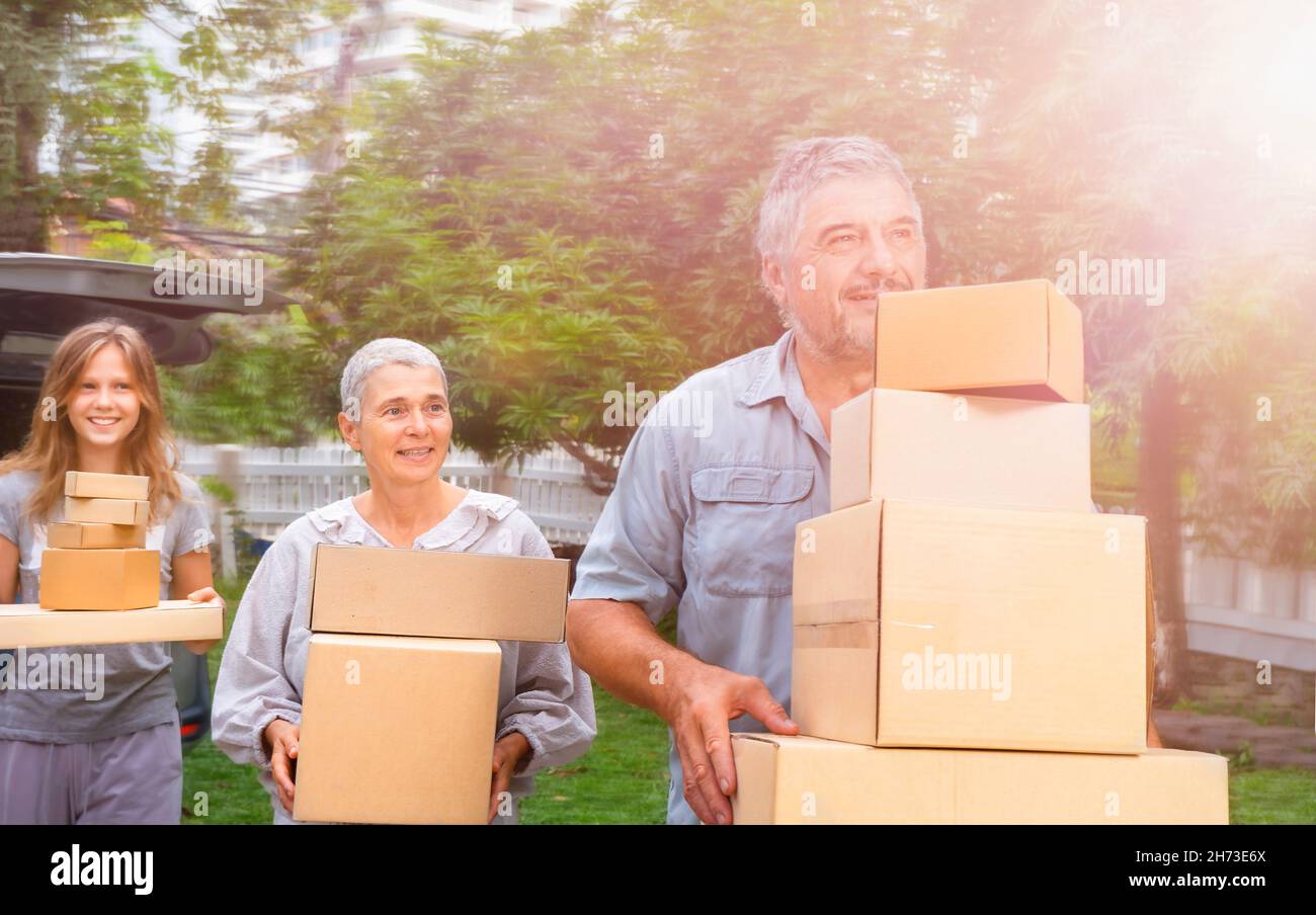 Eine glückliche Familie zieht die Boxen vom Auto in ihr neues Zuhause. Bewegen mit Kartons Stockfoto