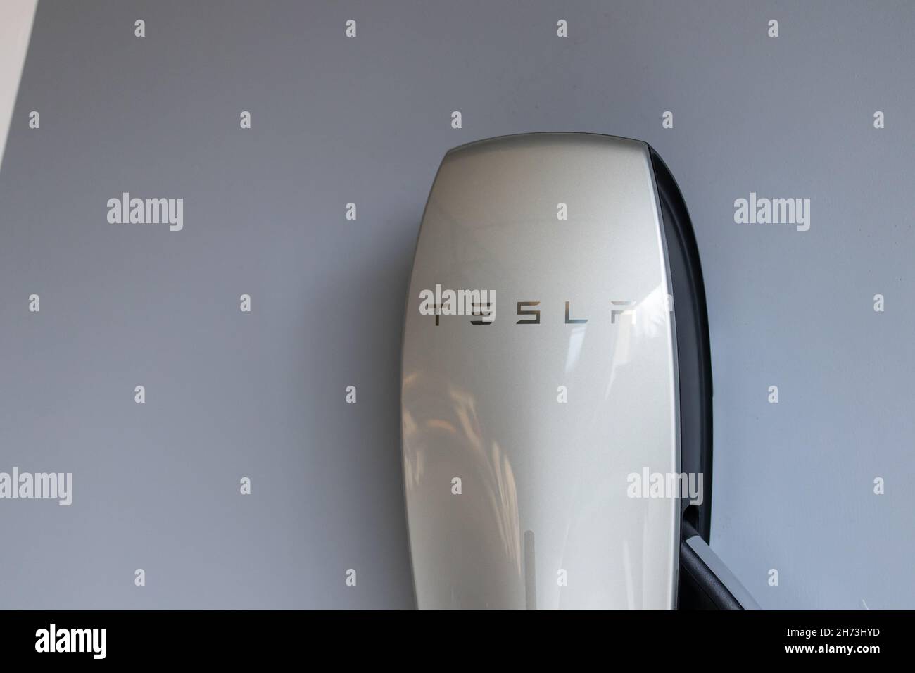 Eine Nahaufnahme eines installierten Tesla-Netzladegeräts, ein verchromtes Tesla-Textlogo auf dem Ladegerät für Elektrofahrzeuge. Stockfoto