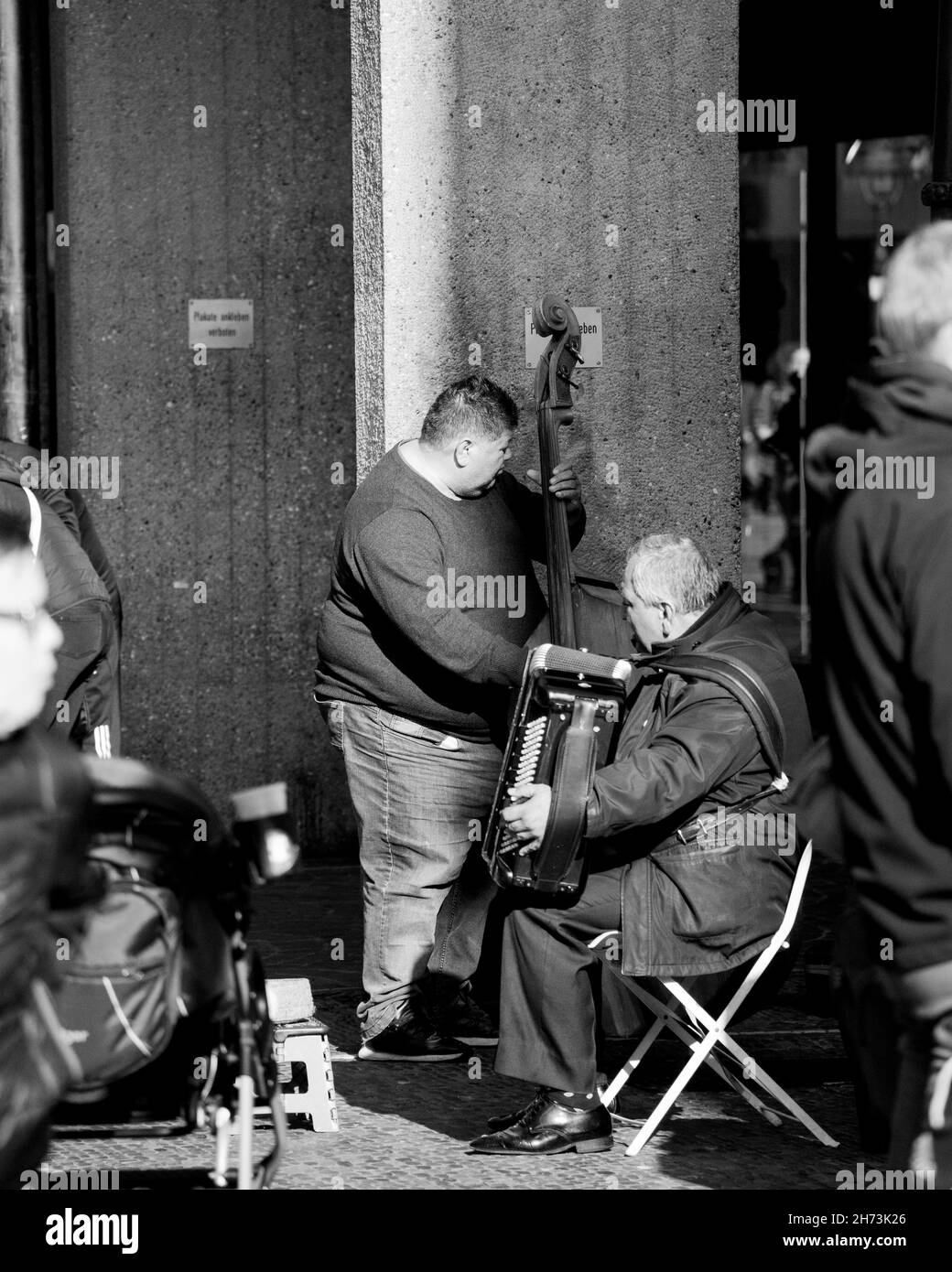 Graustufenaufnahme von zwei Musikern, die auf der Straße Akkordeon und Cello spielen Stockfoto