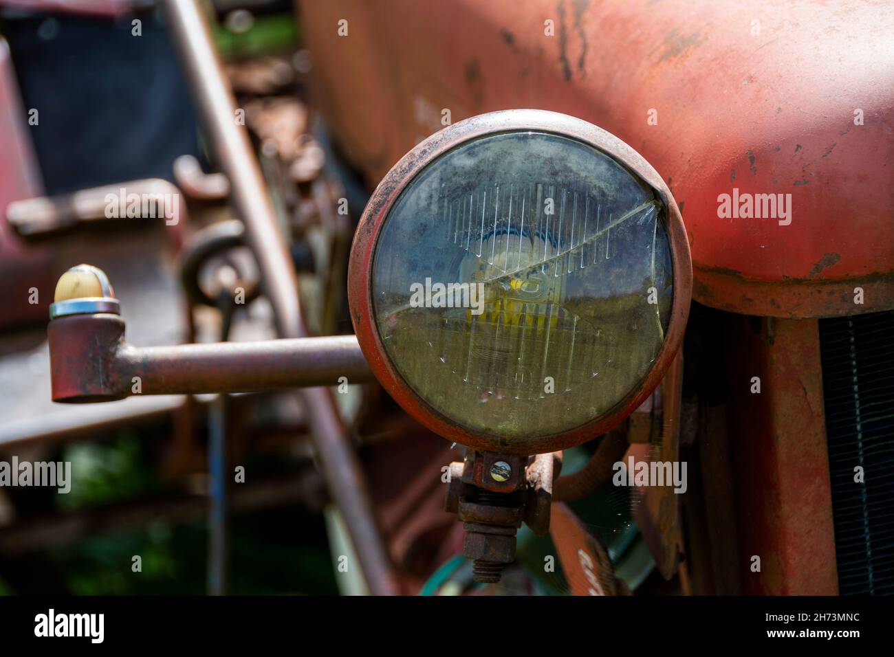 Nahaufnahme eines Oldtimer-Traktorscheinwerfers auf einem Bauernhof während des Tages mit rustikalen Landmaschinen Stockfoto