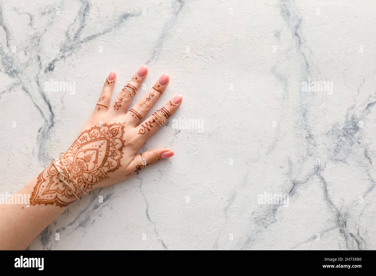 Frau mit Henna bemalten Händen in Ringen und Armbändern auf hellem Marmorhintergrund Stockfoto