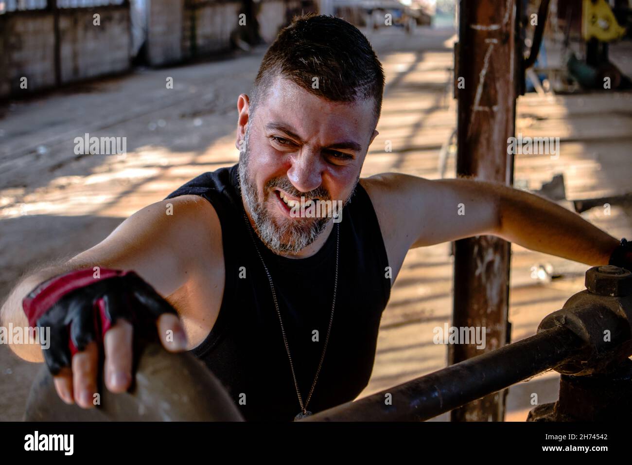 Arbeiter in einer Fabrik am Metallbieger, der Metallstange mit Schutzhandschuhen an einer Presse zusammenklemmend. Altmodische Spannvorrichtung aus Metall. Stockfoto