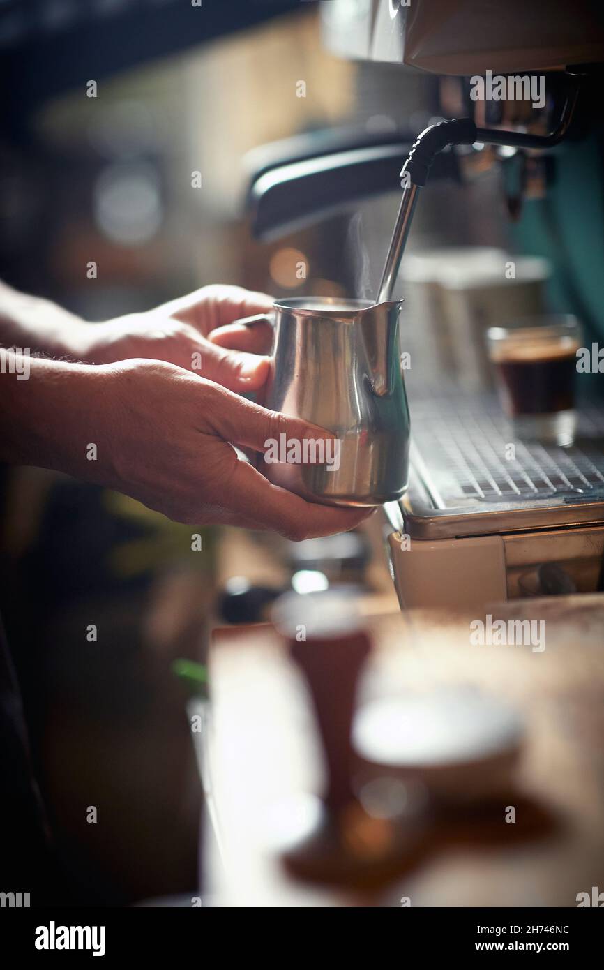 Ein Barkeeper kocht die Milch im Espressomaschine, um sie für ein duftendes Espresso-Getränk zu verwenden. Kaffee, Getränke, Bar Stockfoto