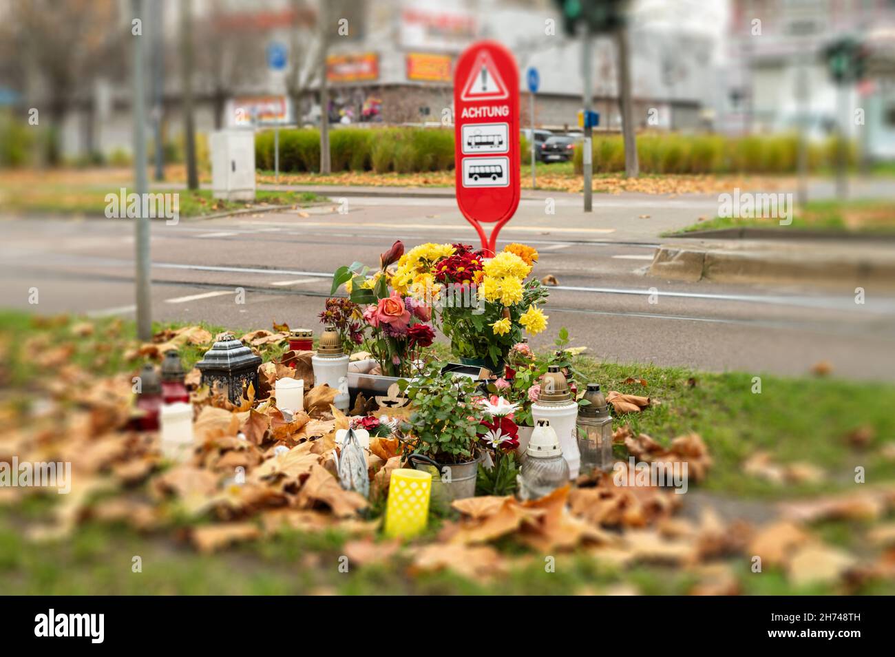 Ein Denkmal für eine tödlich verletzte Person und im Hintergrund ein Warnschild mit der deutschen Aufschrift Achtung Warnung vor der Gefahr durch Busse und Stockfoto