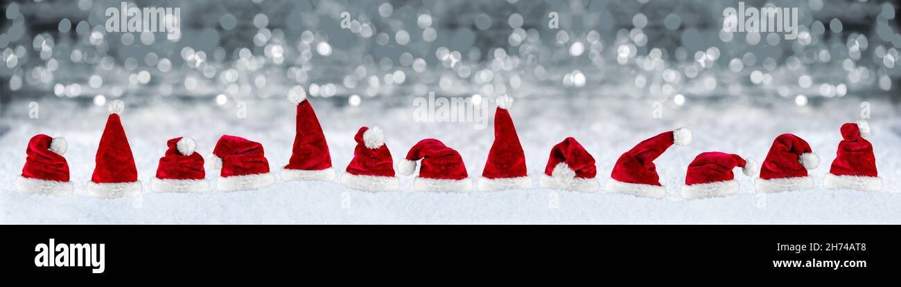 Breite Panorama-Reihe von rot weißen Plüsch weihnachtsmann weihnachtsmütze auf Schnee vor silbergrauen Bokeh Lichter Hintergrund Stockfoto