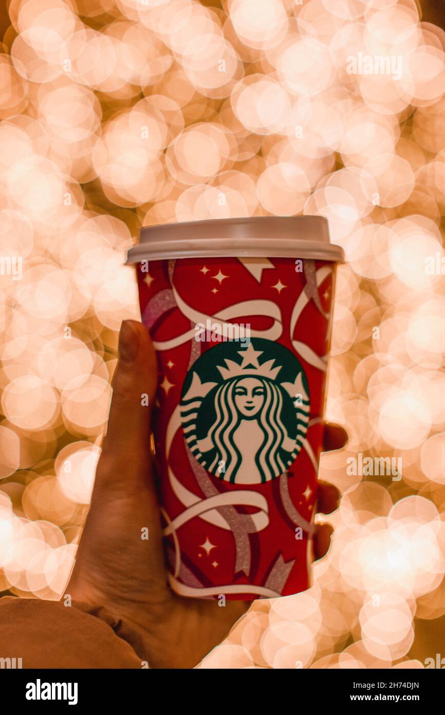 Eine weibliche Hand hält eine Tasse Starbucks-Kaffee zum Neujahr auf einem Hintergrund mit goldenen Bokeh-Weihnachtslichtern Stockfoto