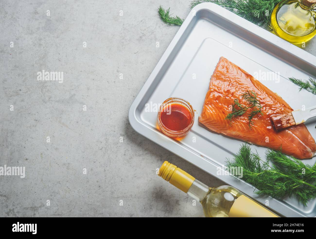 Rohes mariniertes Lachsfilet mit hausgemachter Marinade auf Backblech, Dill, Öl- und Weißweinflasche auf grauem Beton-Küchentisch. Meeresfrüchte Kochen p Stockfoto