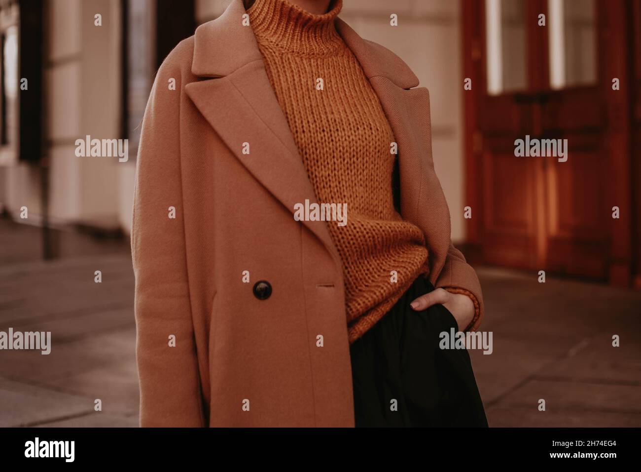 3/4-Frauenfigur in einem braunen, kuschelig warmen Mantel und orangefarbenem Strickpullover. Streetcasual Winter- oder Herbstmode. Stockfoto