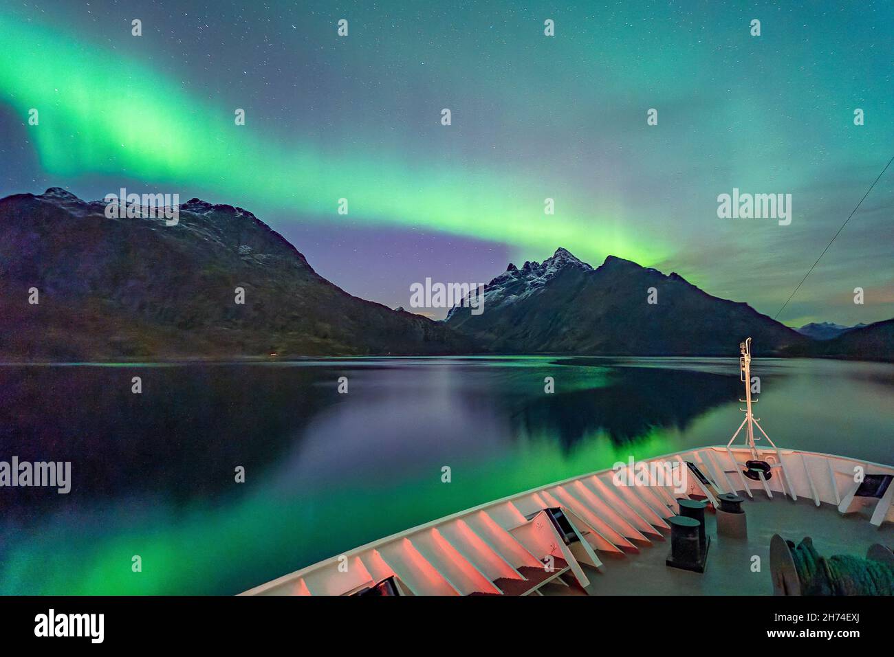 Durch den Raftsund mit dem Postschiff, unter wunderschönen Nordlichtern. tanzende Aurora Borealis in Grün, Gelb und Pink in den Lofoten, Norwegen. Stockfoto