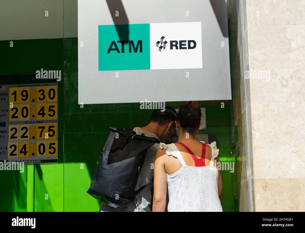 Ein junges Touristenpaar nutzt den Geldautomaten, um Bargeld abzuheben, während es den Geheimcode mit ihren Leichen verschleiert, um Diebstahl in Mexiko zu verhindern. Stockfoto