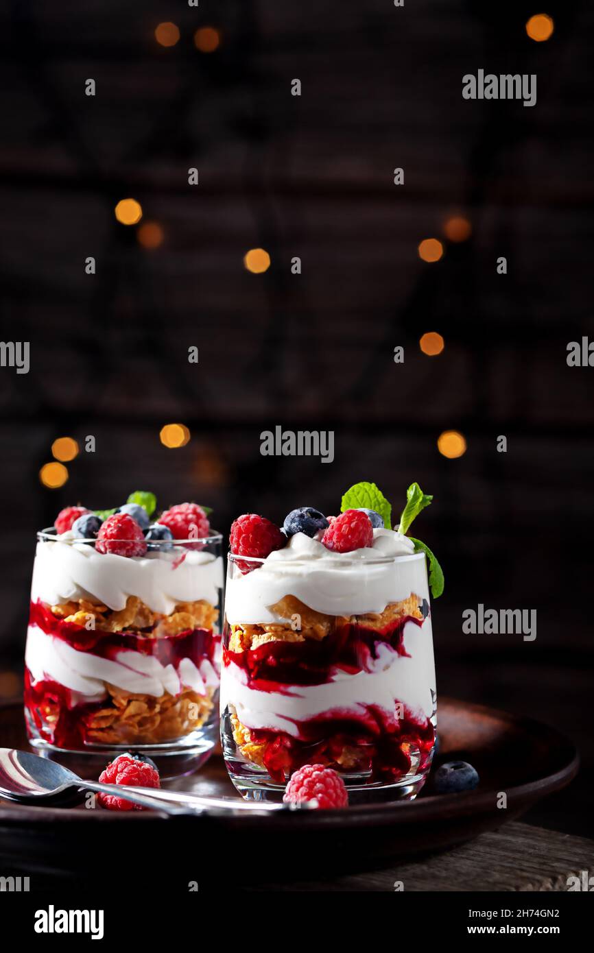 Auf einem hölzernen Hintergrund mit Lichtern, Dessert mit Rahm, Quark, Himbeeren und Heidelbeeren in einem Glas Stockfoto