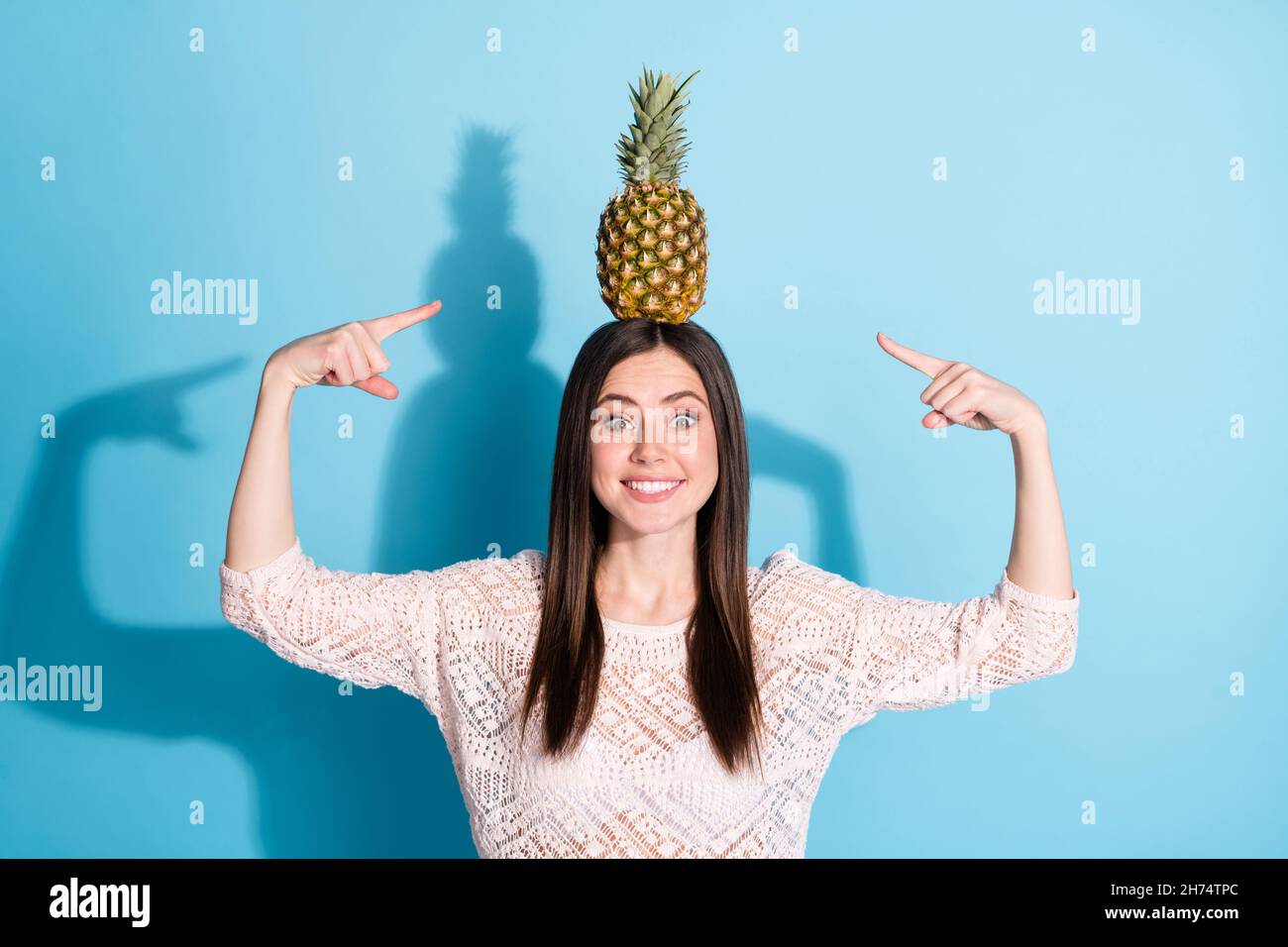 Foto von aufgeregt glücklich nette junge Frau zeigen Finger Ananas auf dem Kopf isoliert auf blauem Hintergrund Stockfoto