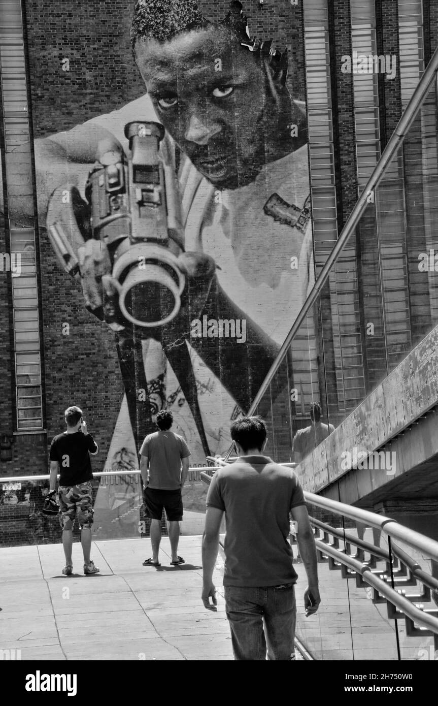 Ein riesiges Plakat, auf dem ein schwarzer Mann mit einem Maschinengewehr abgebildet ist, überblickt Fußgänger auf der Golden Jubilee Bridge in London, Großbritannien. Stockfoto