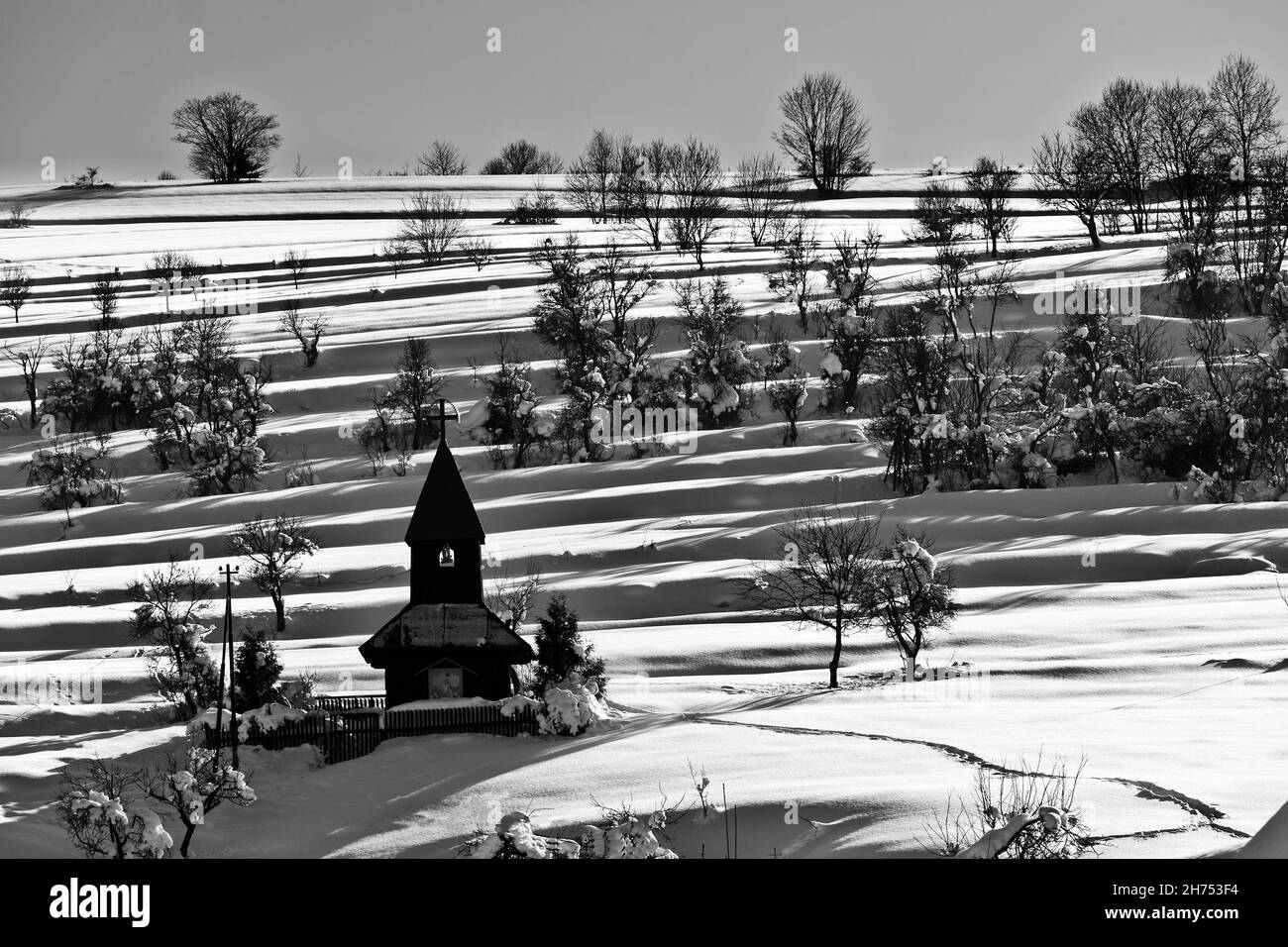 Eine alte Holzkapelle inmitten einer Wiese, unter den Bergen, kaskadierende Felder, Winter, Schnee, Wie in den alten Zeiten, ein verlassener Ort, ein Ort für Stockfoto