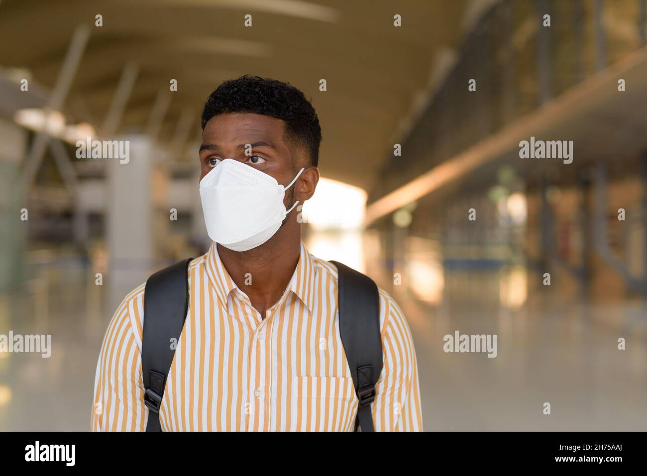 Afrikanischer Mann, der während des Covids am Flughafen unterwegs war und darauf wartete, während er eine Gesichtsmaske trug, während er sich sozial distanzierte Stockfoto