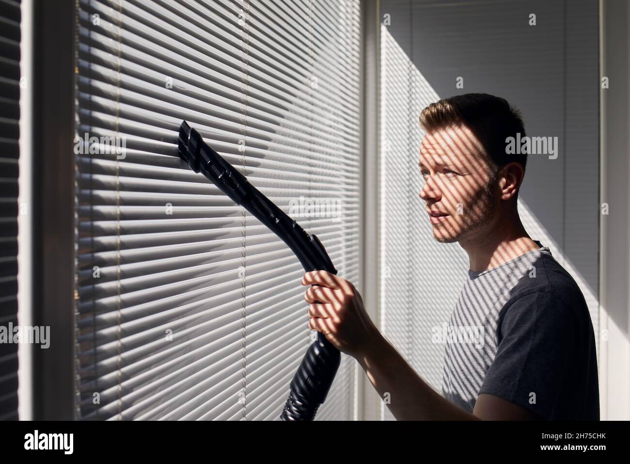 Mann, der zu Hause mit dem Staubsauger Staub von der Fensterblende reinigt. Themen Hausarbeit und Housekeeping. Stockfoto