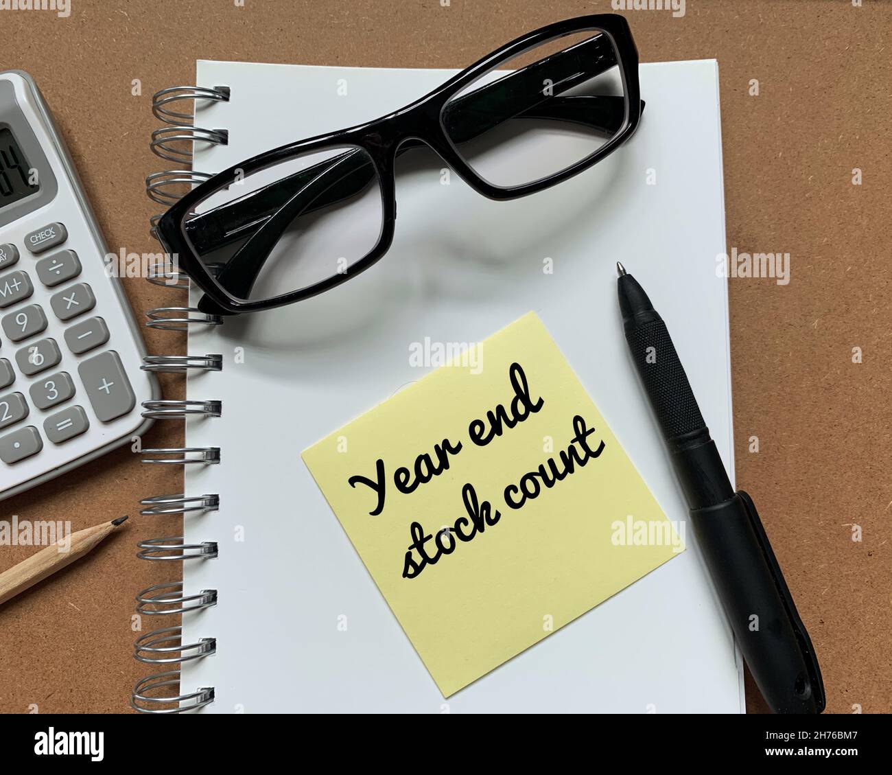 Text zum Jahresabschluss auf Haftnotiz mit Berechnung, Bleistift, Stift und Brille neben einem Notizblock Stockfoto