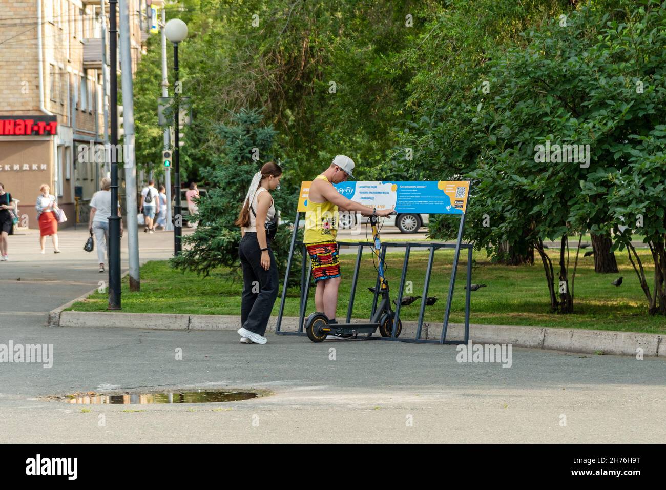 Ein junges Paar mietet sich an einem Sommertag einen Roller über eine Internet-App in einem Stadtpark. Stockfoto